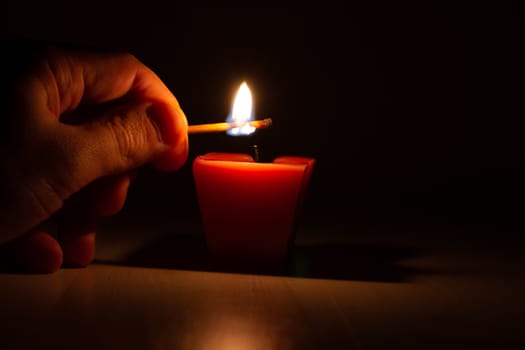 Hand with a match ignites a candle in the dark. Memorable event. Light in the dark. candle in the dark.