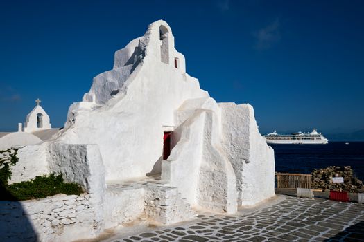 Famous tourist landmark of Greece - Greek Orthodox Church of Panagia Paraportiani in town of Chora on Mykonos island, Greece on sunrise with tourist cruise ship in background