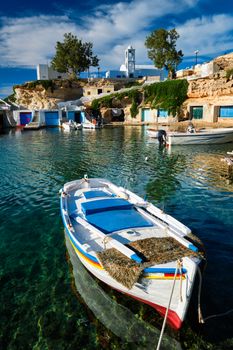 Fishing boats moored in crystal clear turquoise sea water in harbour in Greek fishing village of Mandrakia, Milos island, Greece. Horizontal camera pan