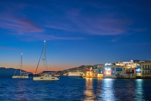 Sunset in Mykonos island, Greece with yachts in the harbor and colorful waterfront houses of Little Venice romantic spot on sunset and cruise ship illuminated in night. Mykonos townd, Greece