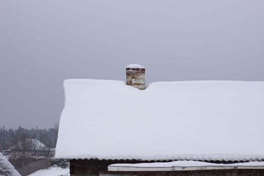 Wooden house in winter in the snow. A house with a chimney and a stove.