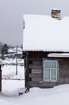 Wooden house in winter in the snow. A house with a chimney and a stove.