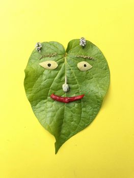 Betel leaf is crafted with flowers and vegetables to represent as a smiling human face with yellow background