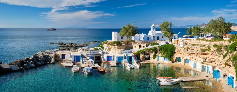 Panorama of typical Greece scenic island view - small harbor with fishing boats in crystal clear turquoise water, traditional white houses church. Mandrakia village, Milos island, Greece.