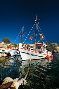 Fishing boats moored in crystal clear turquoise sea water in harbour in Greek fishing village of Mandrakia, Milos island, Greece. Horizontal camera pan