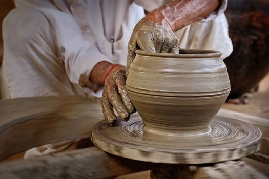 Indian potter at work: throwing the potter's wheel and shaping ceramic vessel and clay ware: pot, jar in pottery workshop. Experienced master. Handwork craft from Shilpagram, Udaipur, Rajasthan, India