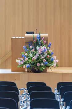 Podium settings with a huge bouquet of flowers on a brown wooden stage ready for lecturers, presenters, speakesman to take place for their speeches 