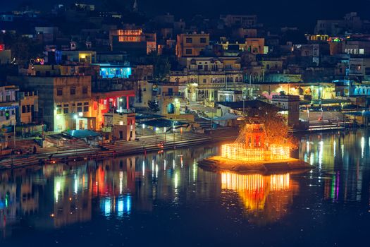 View of famous indian hinduism pilgrimage town sacred holy hindu religious city Pushkar with Brahma temple, aarti ceremony, lake and ghats illuminated at sunset. Rajasthan, India. Horizontal pan