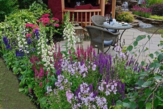 The patio area of an aquatic garden with colourful flower border with Summer House and outdoor eating on the terrace,
