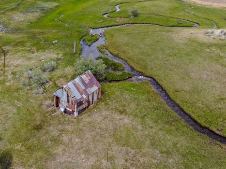 Aerial view of abandoned little small wooden house barn next small river in the green valley of a mountain, Aspen Spring, Mono County, California, USA. 