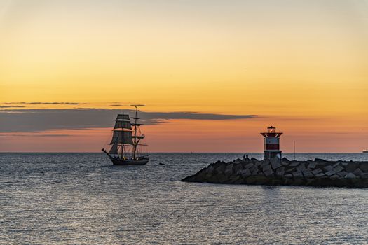Tall ship, vessel, sailing and preparing the enter inside the harbor of Scheveningen at the vivid sunset moment, The Hague, Netherlands