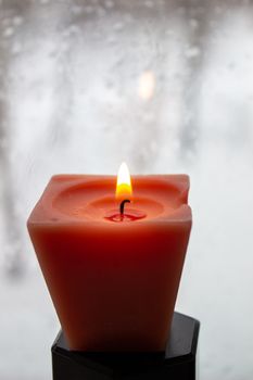 Candle burning near a frosted window in twilight. Winter evening