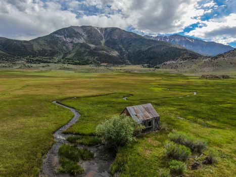 Aerial view of abandoned little small wooden house barn next small river in the green valley of a mountain, Aspen Spring, Mono County, California, USA. 