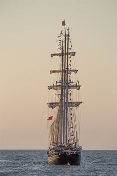 Antique tall ship, vessel leaving the harbor of The Hague, Scheveningen under a warm sunset and golden sky