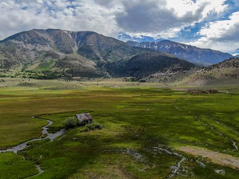 Aerial view of abandoned little small wooden house barn next small river in the green valley of a mountain, Aspen Spring, Mono County, California, USA. 