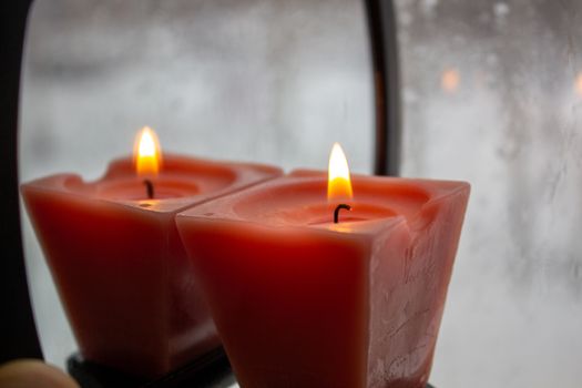 Candle burning near a frosted window in twilight. Winter evening