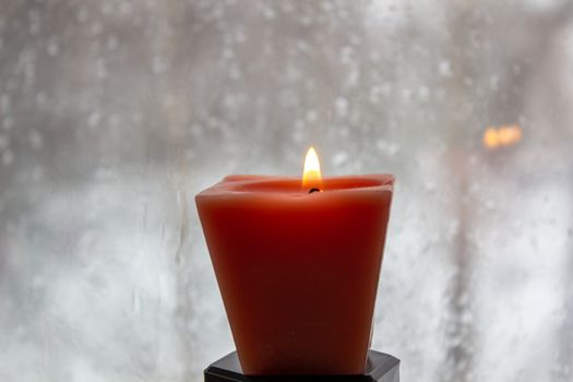 Candle burning near a frosted window in twilight. Winter evening