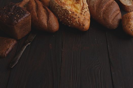 Different wholegrain breads on burnished wooden table. Elevated view, chiaroscuro styled