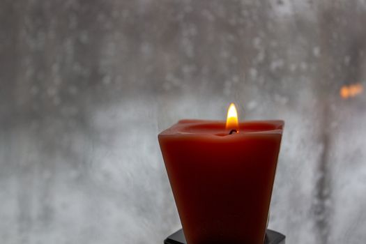 Candle burning near a frosted window in twilight. Winter evening