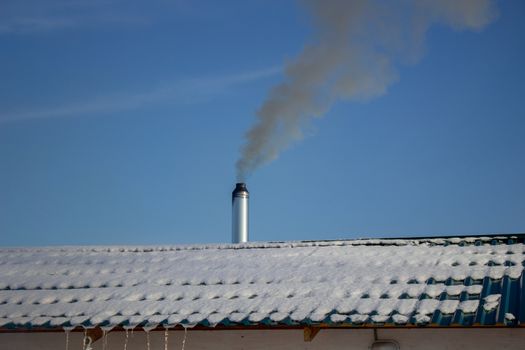 Modern steel chimney of a Russian sauna covered with snow against a blue sky