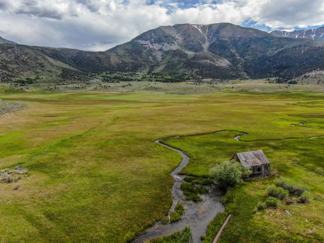 Aerial view of abandoned little small wooden house barn next small river in the green valley of a mountain, Aspen Spring, Mono County, California, USA. 