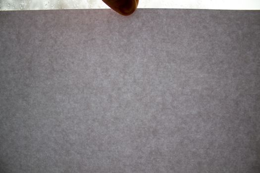A man holds a grey cardboard page against the background of a window