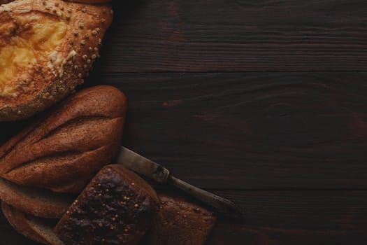 Different wholegrain breads on burnished wooden table. Flat lay, above view, chiaroscuro styled