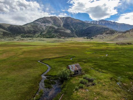 Aerial view of abandoned little small wooden house barn next small river in the green valley of a mountain, Aspen Spring, Mono County, California, USA. 