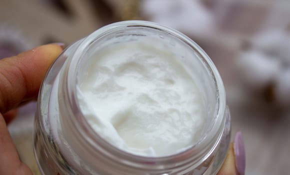 Closeup of young woman's hand holding jar of moisturizing cream in hands.