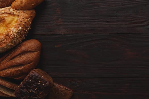 Different wholegrain breads on burnished wooden table. Flat lay, above view, chiaroscuro styled