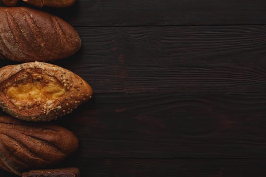 Different wholegrain breads on burnished wooden table. Flat lay, above view, chiaroscuro styled