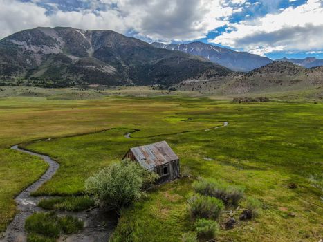 Aerial view of abandoned little small wooden house barn next small river in the green valley of a mountain, Aspen Spring, Mono County, California, USA. 