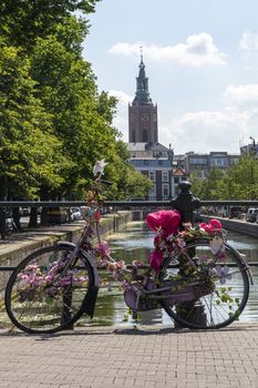 Pink bicycle parking on a bridge over the calm canal against a brick made church in The Hague, Netherlands