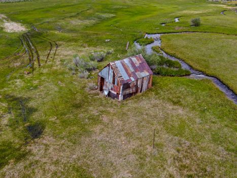 Aerial view of abandoned little small wooden house barn next small river in the green valley of a mountain, Aspen Spring, Mono County, California, USA. 