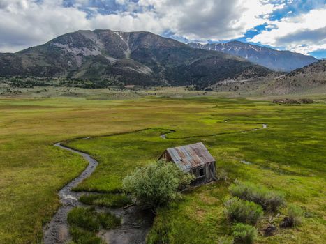 Aerial view of abandoned little small wooden house barn next small river in the green valley of a mountain, Aspen Spring, Mono County, California, USA. 