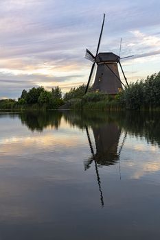 Dutch windmill reflected on the calm canal water at the early sunset lights