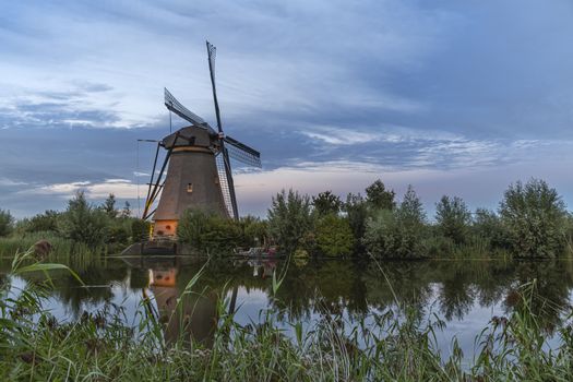 Dutch windmill reflected on the calm canal water at the early sunset lights