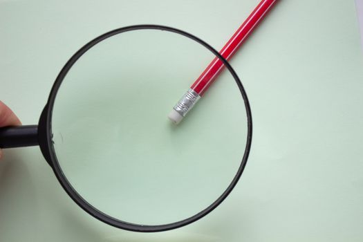 One red pencil under a magnifying glass close-up on a light background