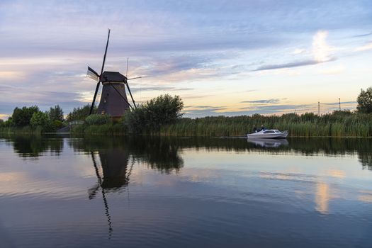 Dutch windmill laying along the canal with wild grass blown by strong winds at the early sunset moment