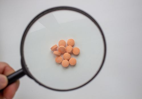 Medical tablets under a magnifying glass on a white background