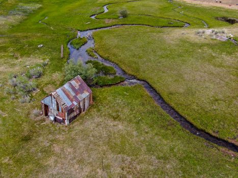 Aerial view of abandoned little small wooden house barn next small river in the green valley of a mountain, Aspen Spring, Mono County, California, USA. 