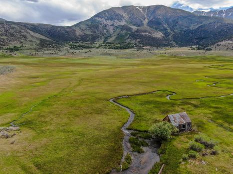 Aerial view of abandoned little small wooden house barn next small river in the green valley of a mountain, Aspen Spring, Mono County, California, USA. 