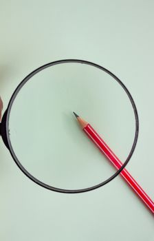 One red pencil under a magnifying glass close-up on a light background