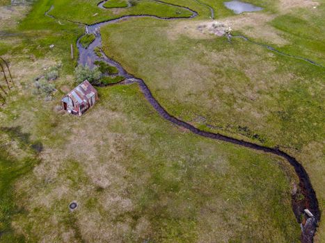 Aerial view of abandoned little small wooden house barn next small river in the green valley of a mountain, Aspen Spring, Mono County, California, USA. 