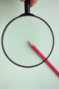 One red pencil under a magnifying glass close-up on a light background