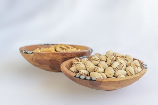 Chestnuts and pistachios in wooden bol as appertiser with drinks against a white background