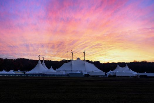 Circus tent under a warn sunset and chaotic sky without the name of the circus company which is cloned out and replaced by the metallic structure