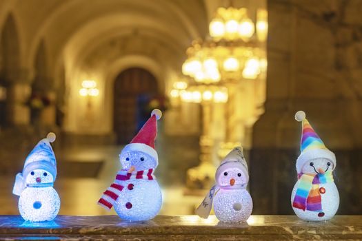 Little snowman wearing a rainbow scarf and hat against a golden light bokeh waiting for Christmas time and gifts