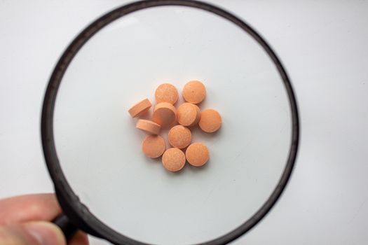 Medical tablets under a magnifying glass on a white background