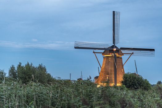 Dutch windmill above the fence of wild grass blown by strong winds during the blue hour, Alblasserdam, Netherlands